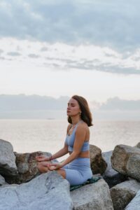 Woman meditating on rocks by the sea during a tranquil sunset, embracing peace.